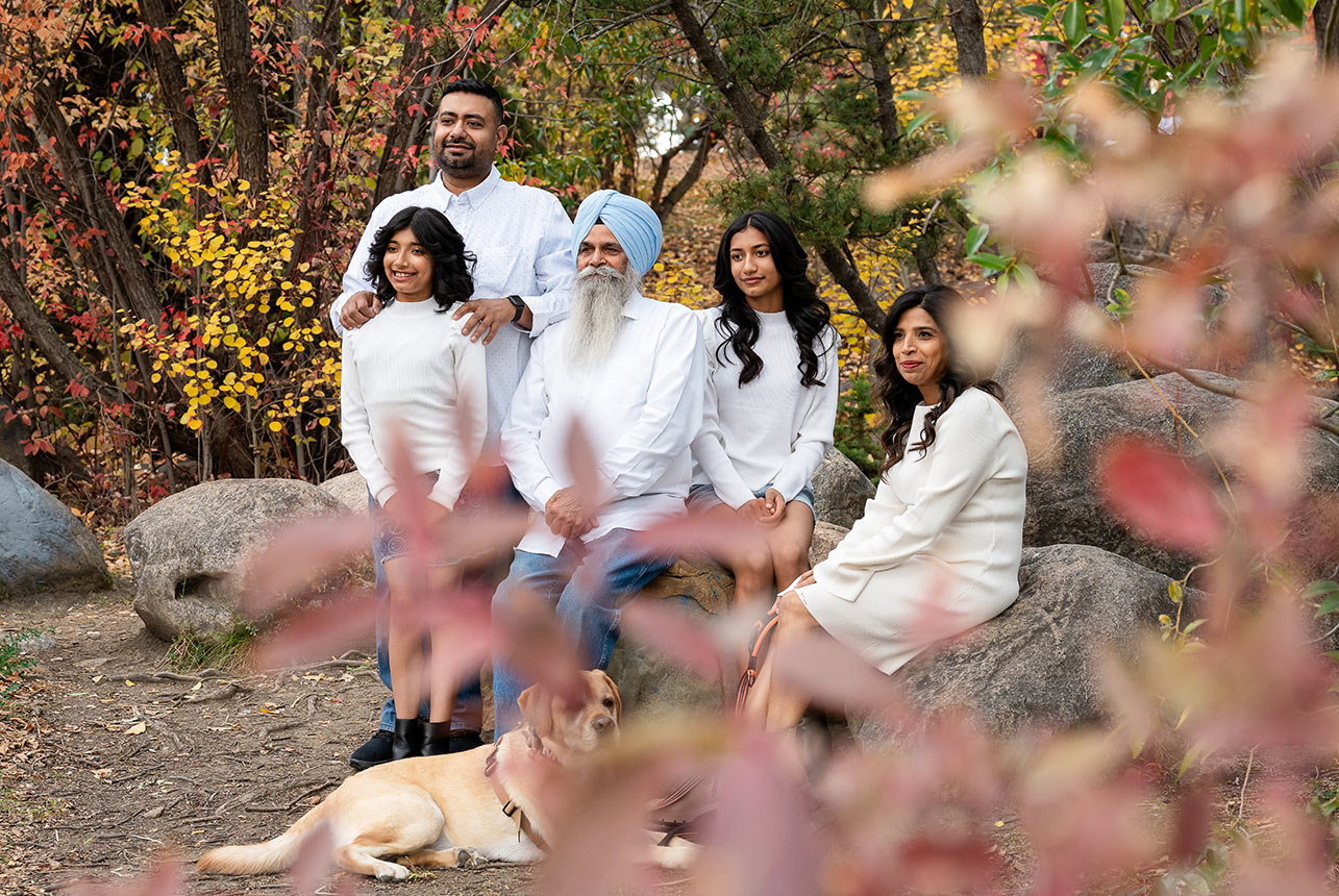 Multigenerational family with dog posing on rocks surrounded by vibrant fall trees at Beaumaris Lake