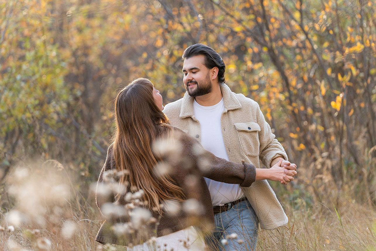 Couple dance in tall grasses, smiling at each other with hands linked in warm autumn light
