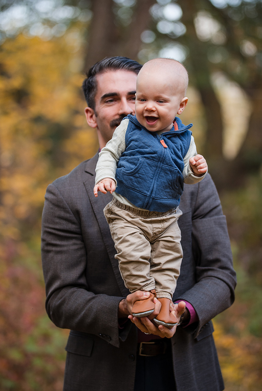 Baby boy balanced standing in Dad's hands with a smile of achievement.