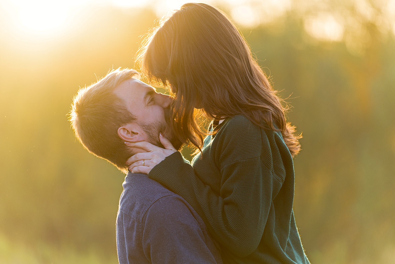 Couple share a backlit kiss at sunset, warm golden glow around their faces