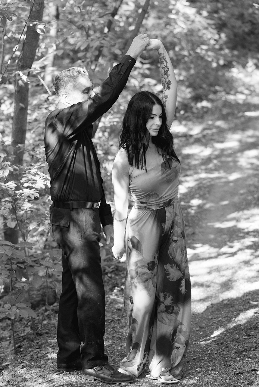 Black and white photo of engaged couple mid-spin on forest path in Edmonton