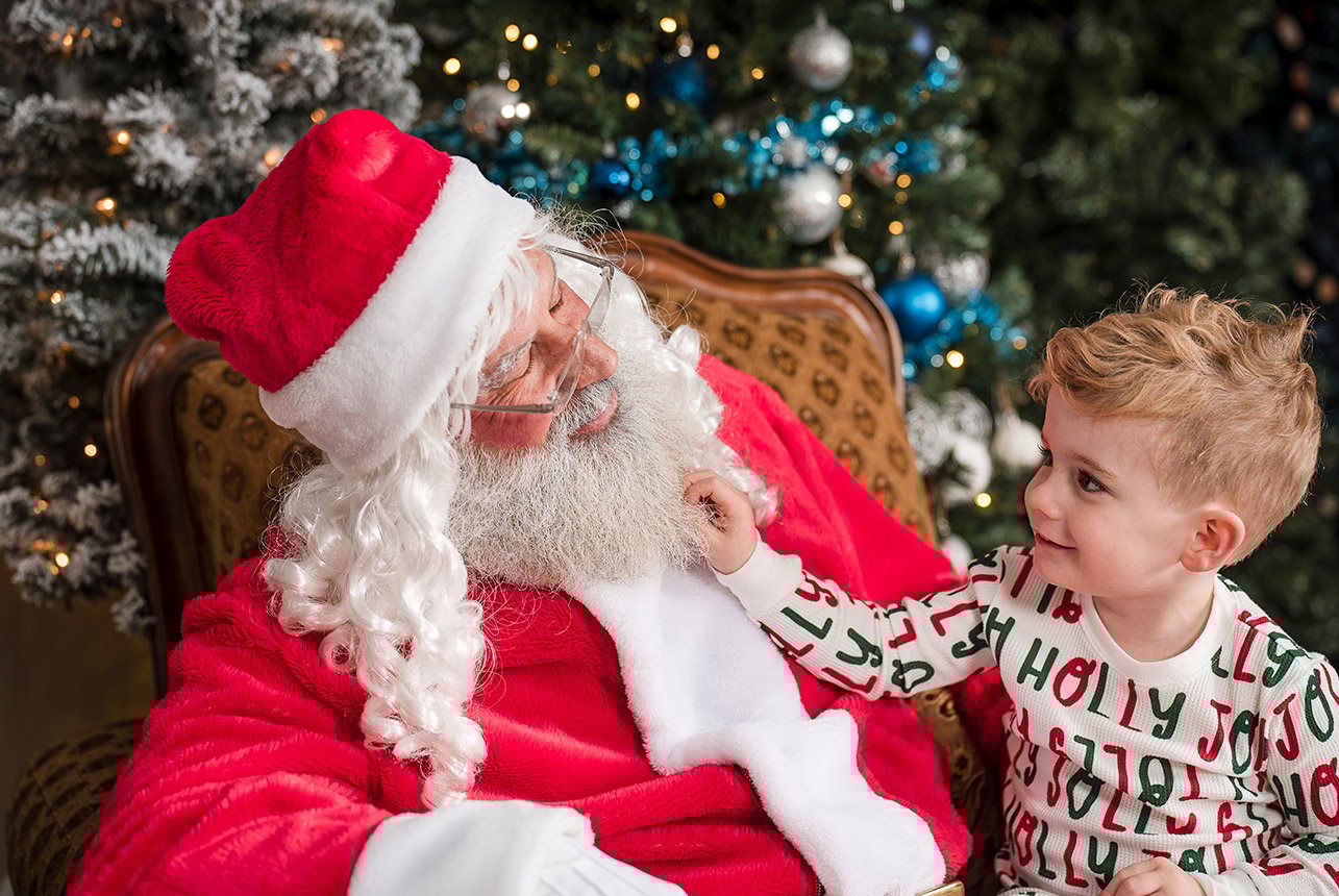 Joyful boy pulling Santa's beard during a Christmas photo session.