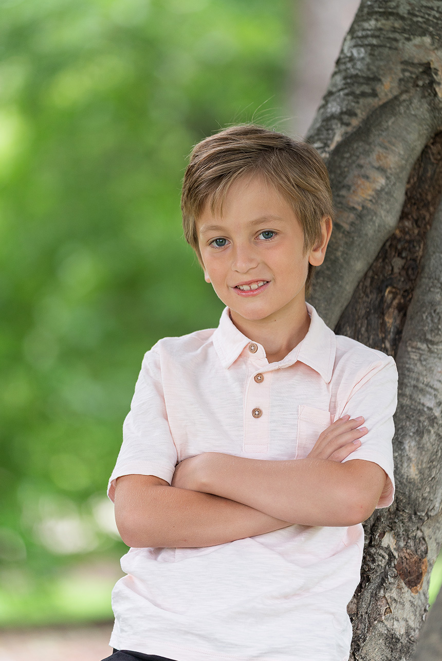 Young boy leaning against tree in summer portrait at Smeltzer House