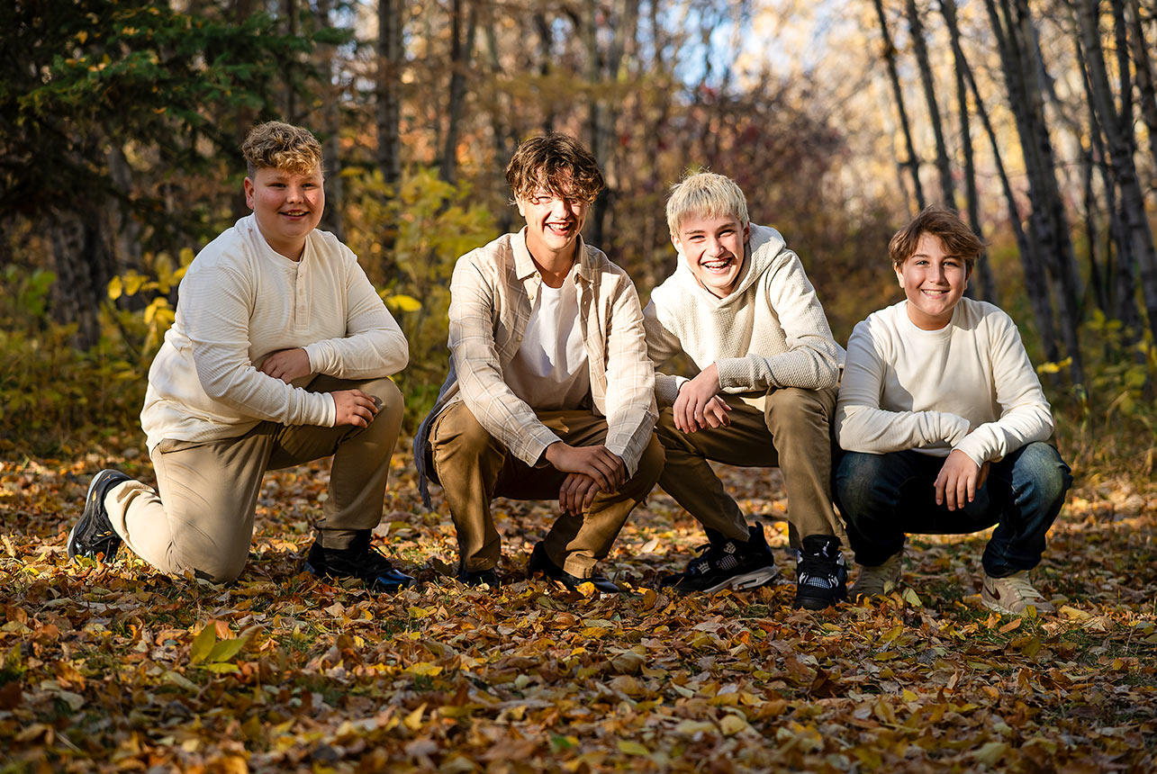 Four boys smiling and kneeling on fallen leaves during a golden autumn photo shoot