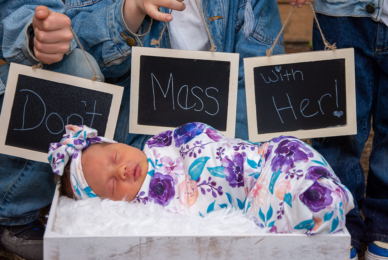 boys-with-sign-don’t-mess-with-her-newborn Three Siblings Admiring Their Newborn Sister in a Basket with a Cute Warning Sign