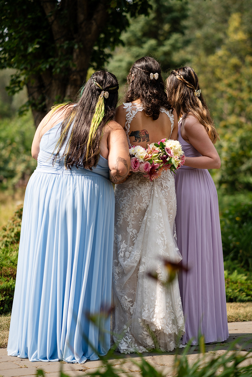 Bride and bridesmaids with arms locked from behind, holding bouquets at the bride's waist during their wedding ceremony.
