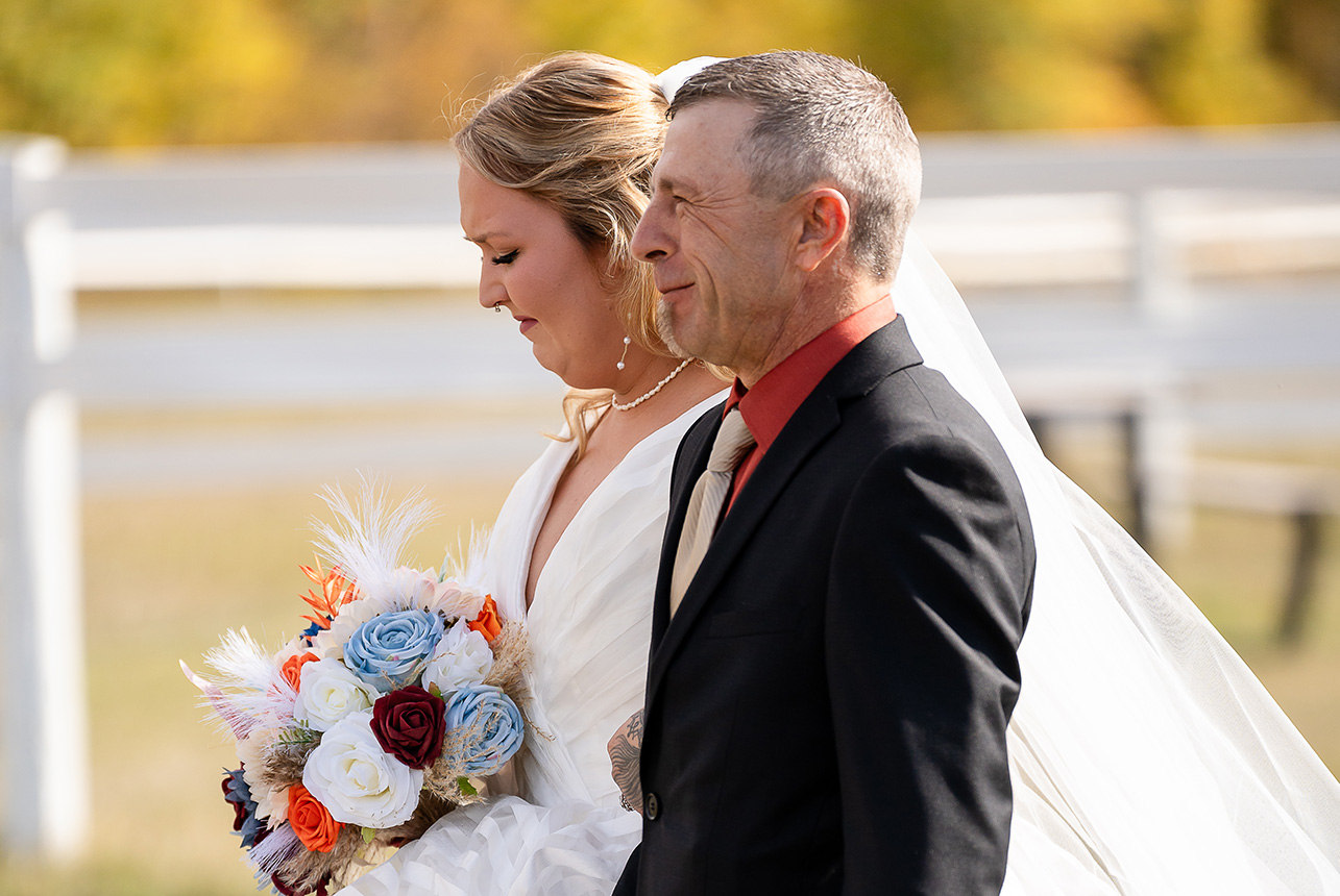 Close-up of the bride, emotional and teary, holding her bouquet with stunning autumn leaves blurred in the background