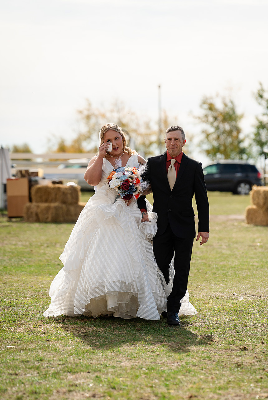 Bride sheds a tear while walking with her father down the wedding aisle at Finnegan Farms on a sunny autumn day