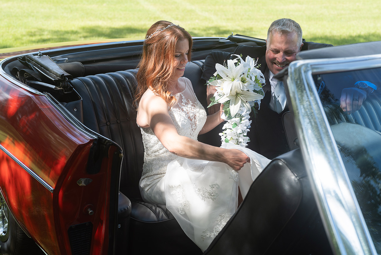 Bride and groom sitting in backseat of vintage red Impala laughing