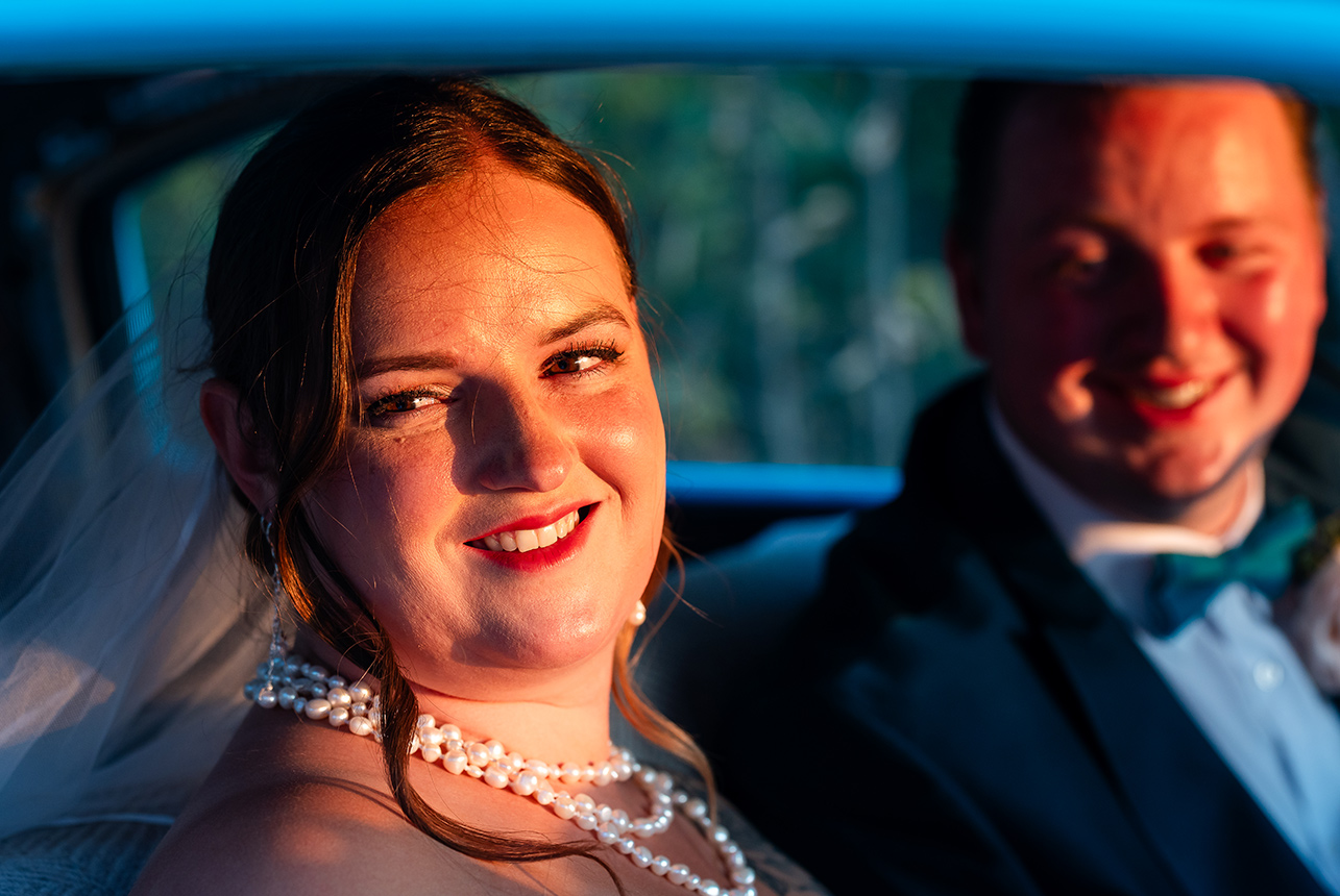 Bride and groom pause inside their car, bathed in the golden glow of the setting sun, sharing a quiet and intimate moment