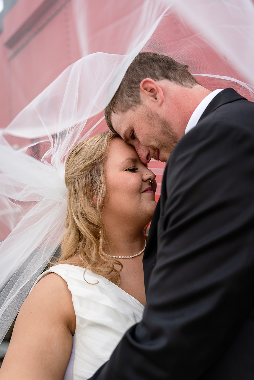 Bride and groom under a flowing veil, with the groom opening his eyes as though in a dream, and the CN red caboose in the background.