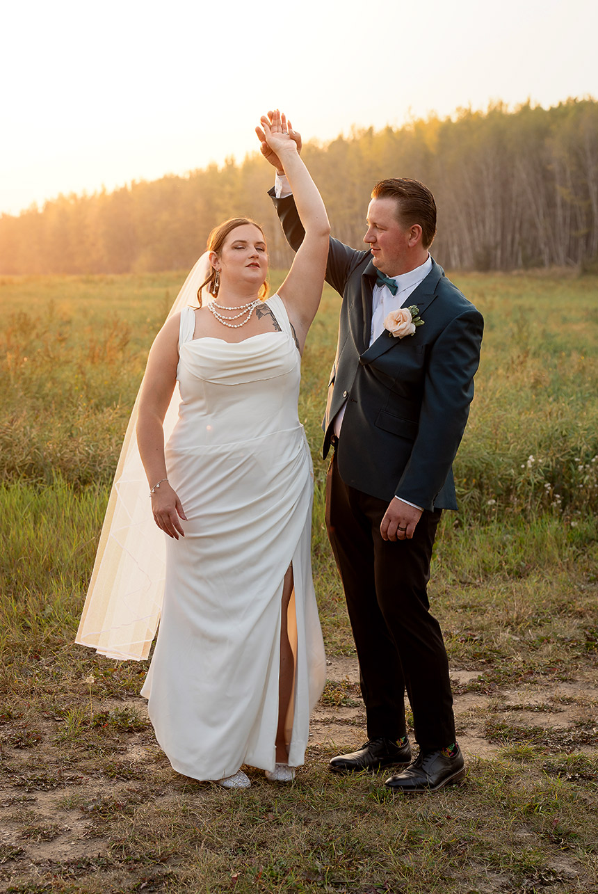 Bride and groom share their first dance in an open field as the golden sun sets behind them, casting a romantic glow