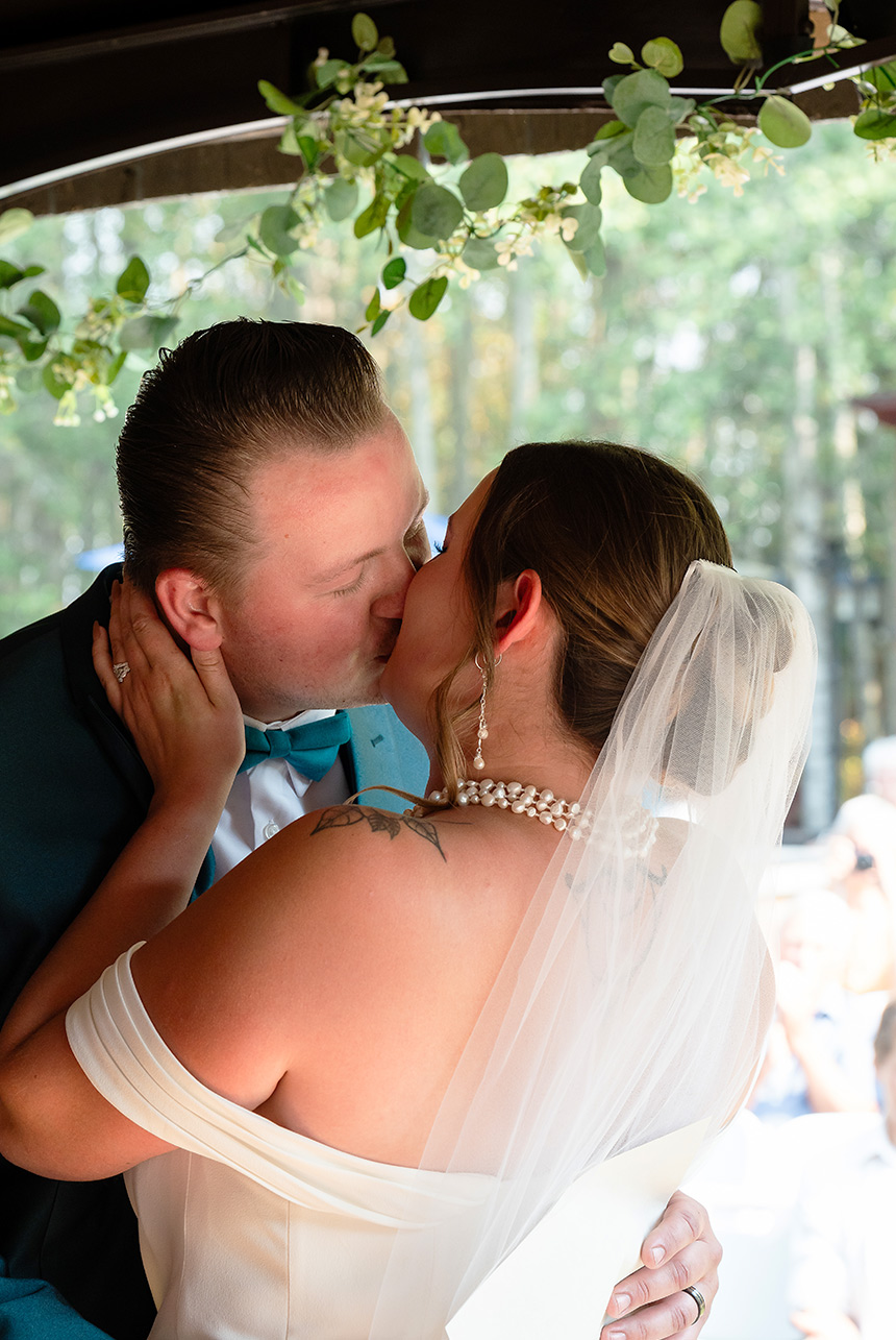 Bride and groom share their official first kiss on the ceremony stage, holding each other close as guests look on