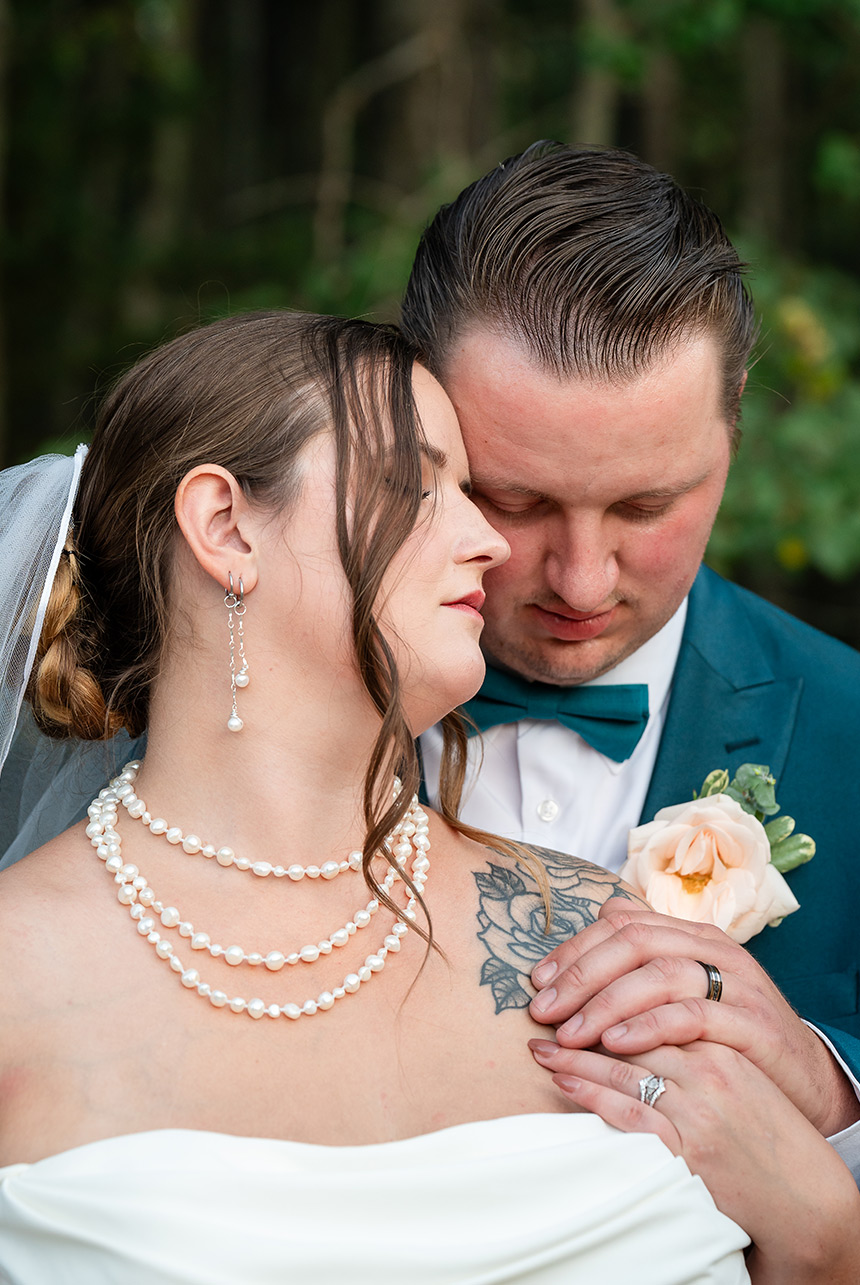 Bride and groom gently place their hands on her shoulder, their new wedding rings shining in the soft light of the evening