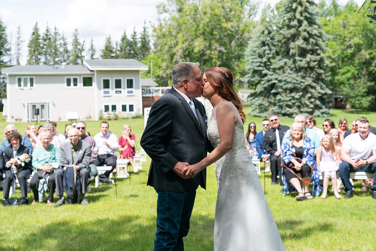 Bride and groom share first kiss in front of wedding guests outdoors
