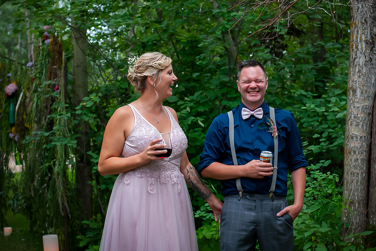 Bride and groom laughing with drinks in hand at their backyard wedding