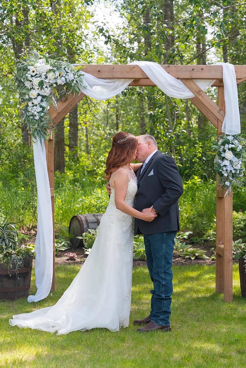 Bride and groom share a long kiss beneath rustic floral arch