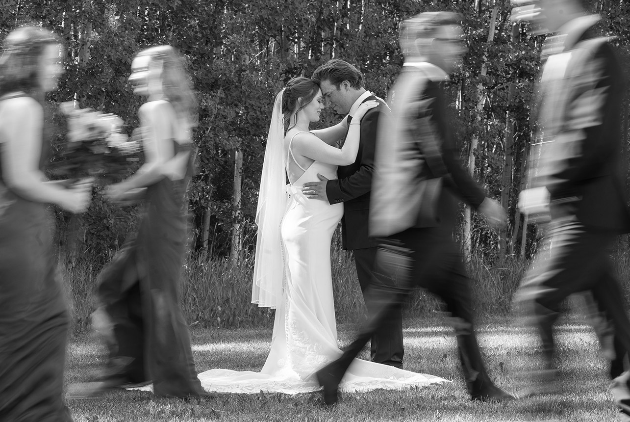 Bride and groom share a quiet moment as wedding party walks past in motion blur