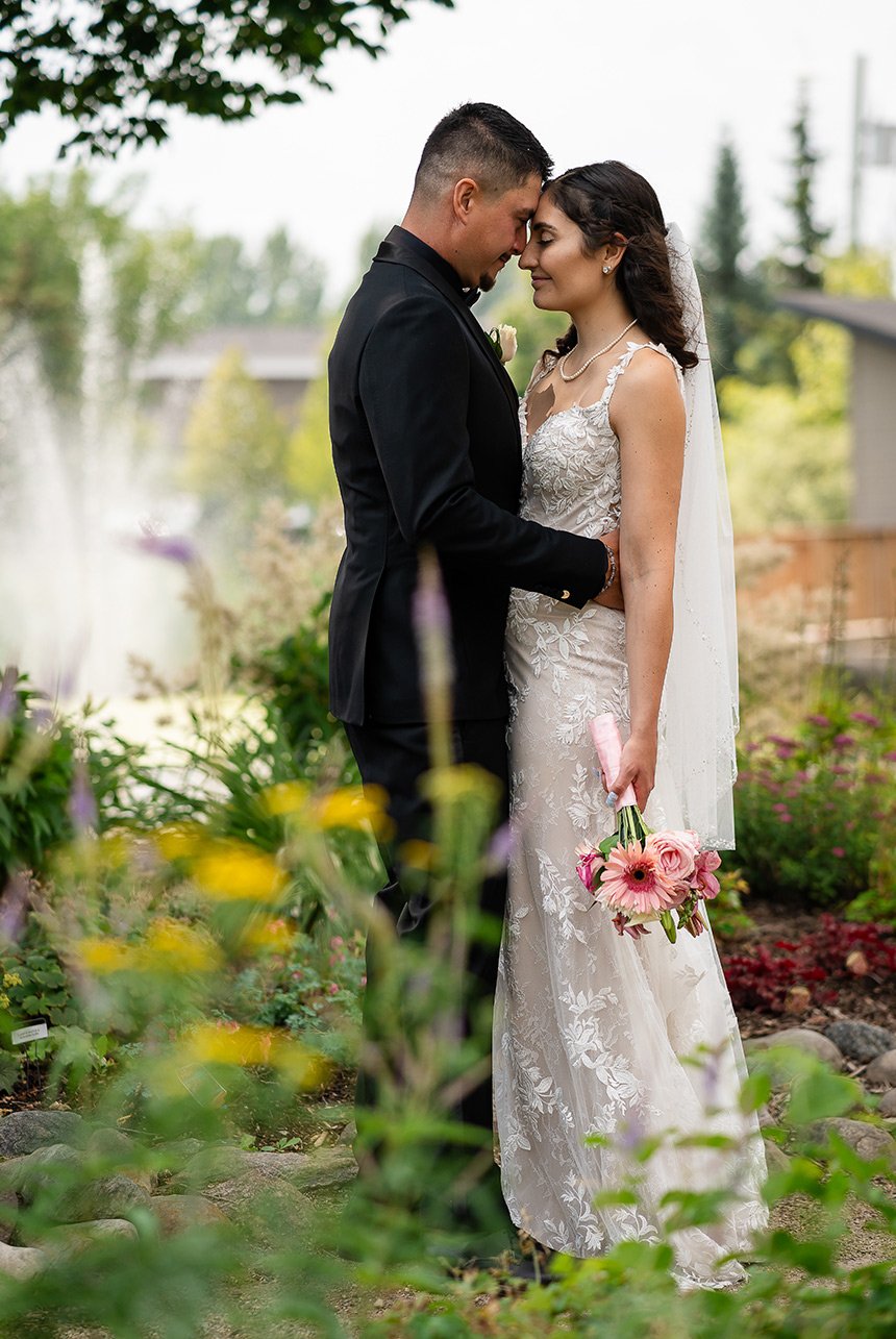 Bride and groom standing in the middle of the gardens, exuding tranquil peace with a water fountain in the blurred backdrop.