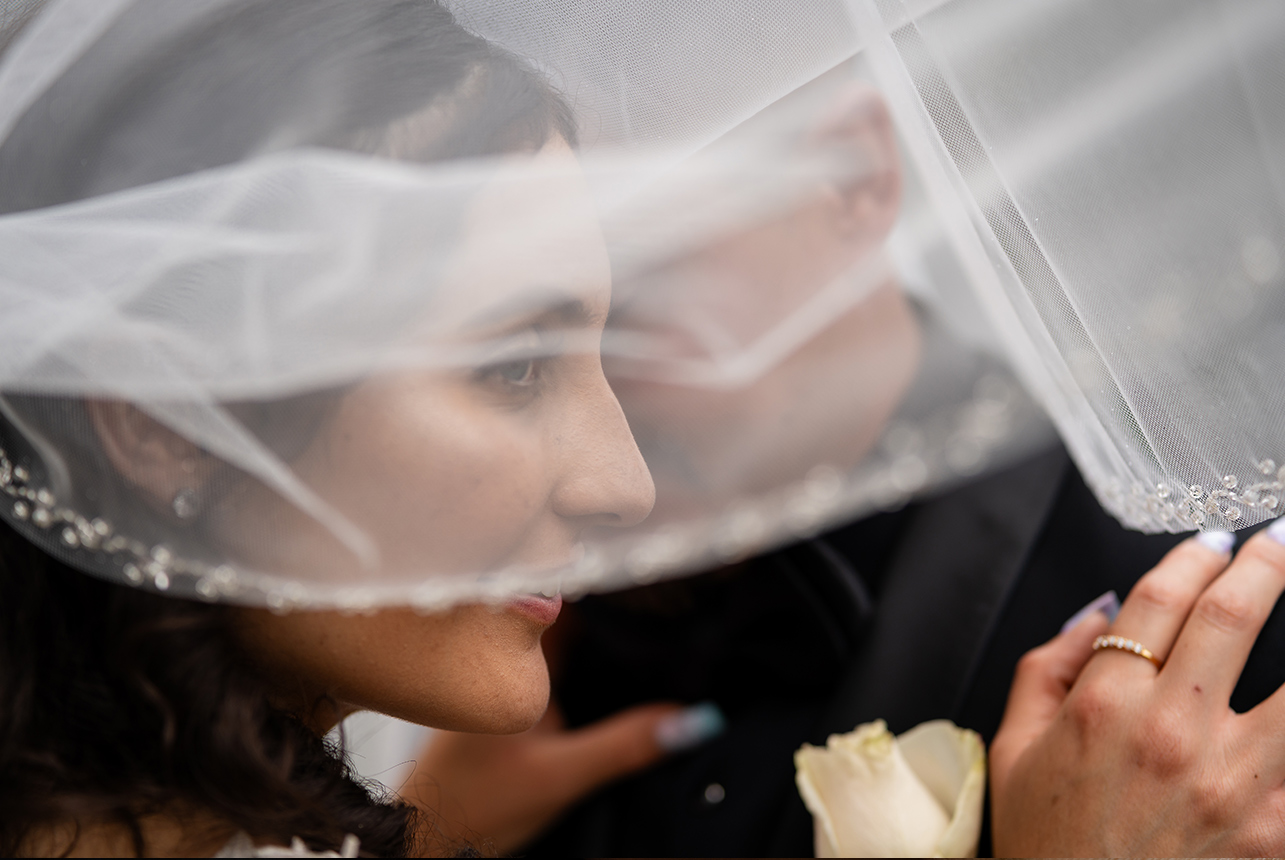 Bride and groom standing under the bride's veil, with the bride gazing towards her side shoulder.