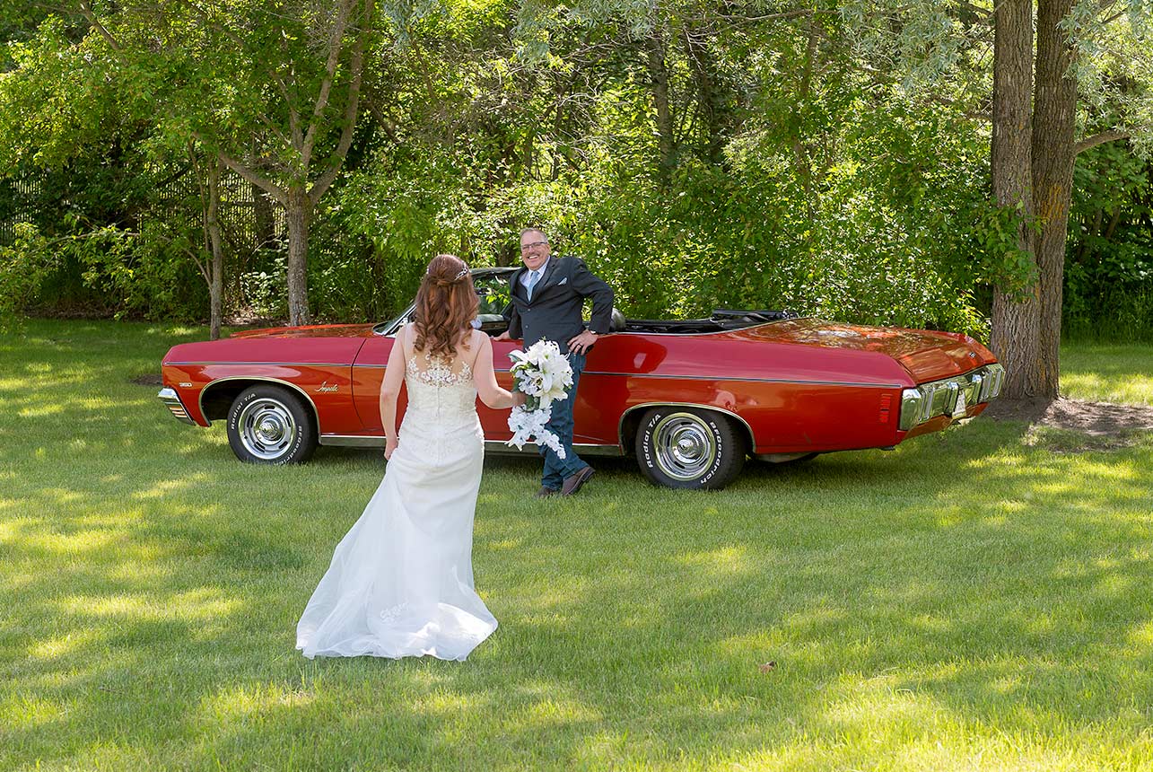 Bride walking toward groom leaning on vintage red Impala