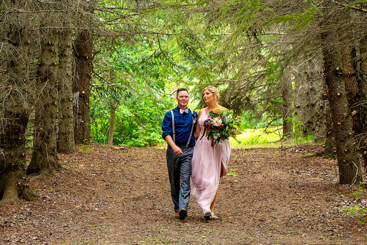 Bride and groom walking arm in arm through pine forest trail