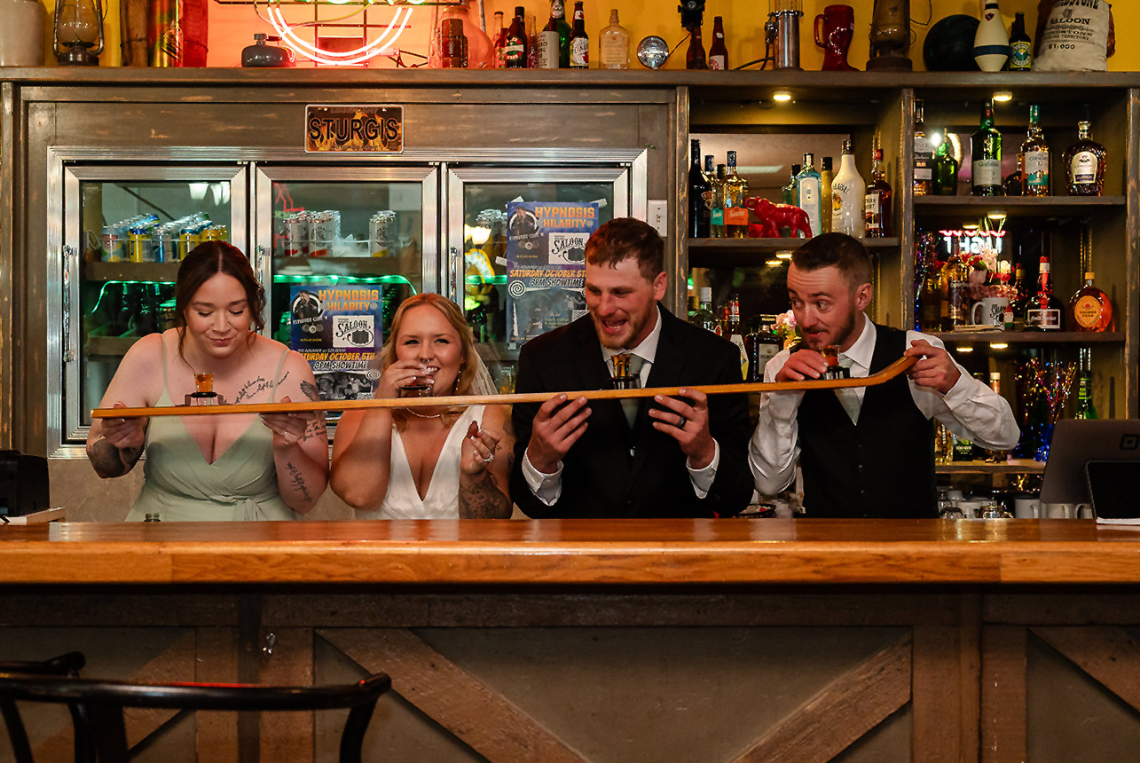 Bride, groom, best man, and bridesmaid take shots together using a shotski at Kicks Saloon Bar in Redwater, Alberta