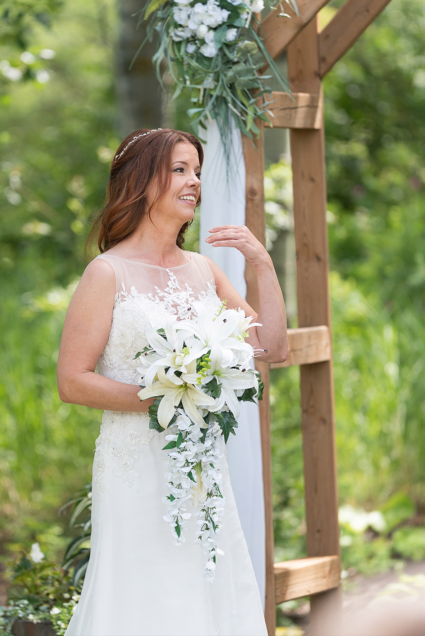 Bride holding cascading white lily bouquet under ceremony arch