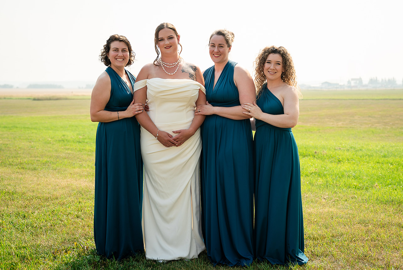 Bride, maid of honor, and bridesmaids stand in an open pasture, their dresses flowing in the breeze as they pose together