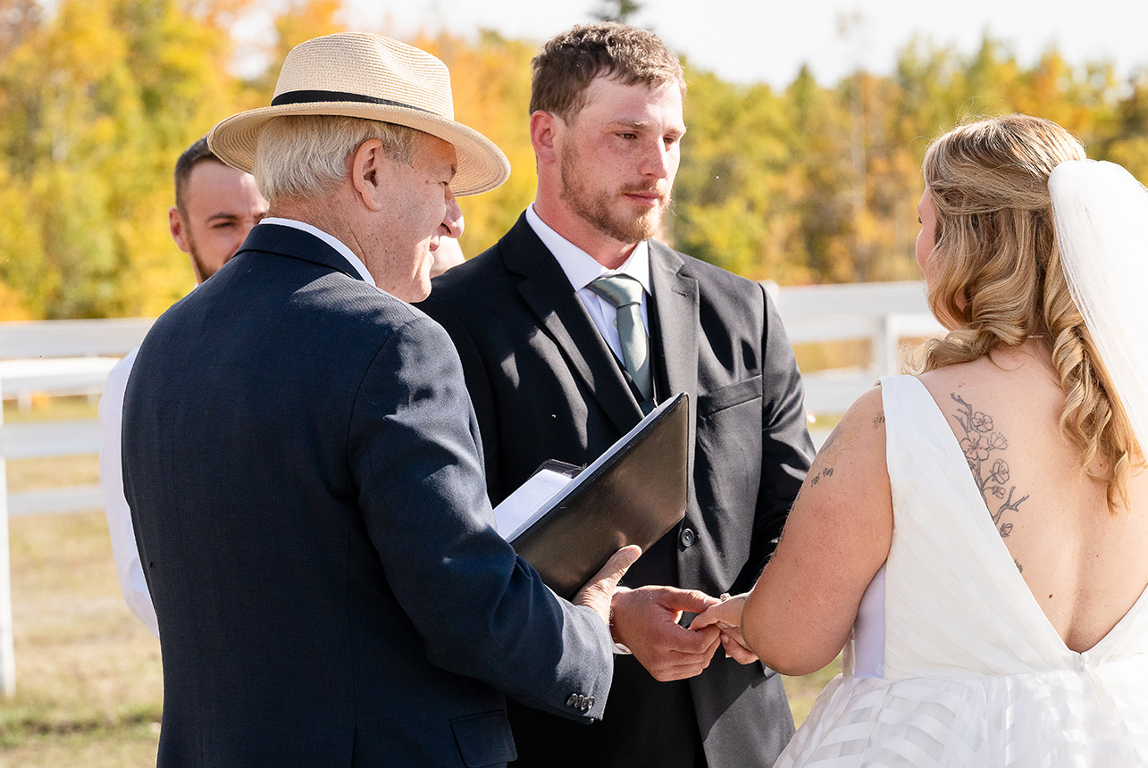 Groom slides a ring onto the bride’s finger during the ceremony, with the autumn backdrop at Finnegan Farms