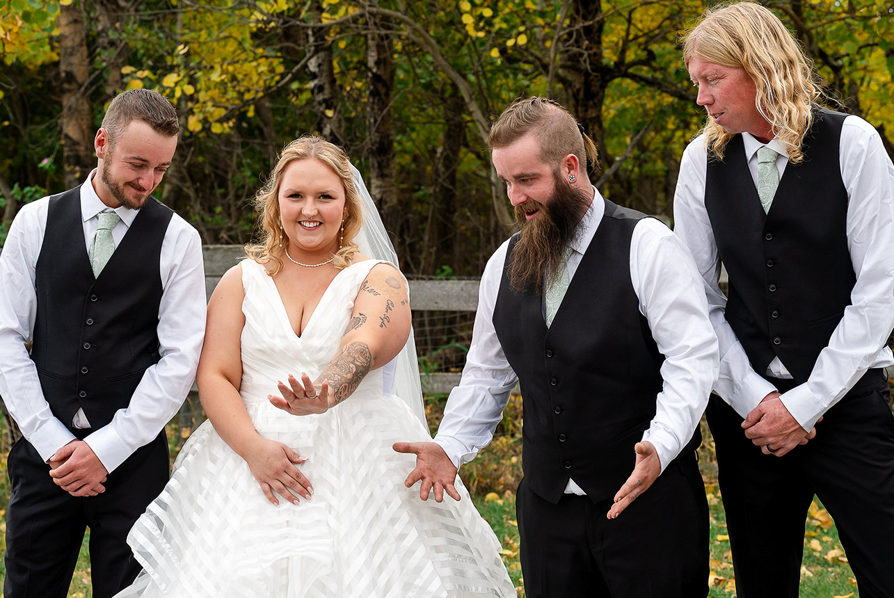 Bride shows off her wedding ring as the groomsmen surround her with playful, wow expressions during the celebration, set against a rustic autumn backdrop