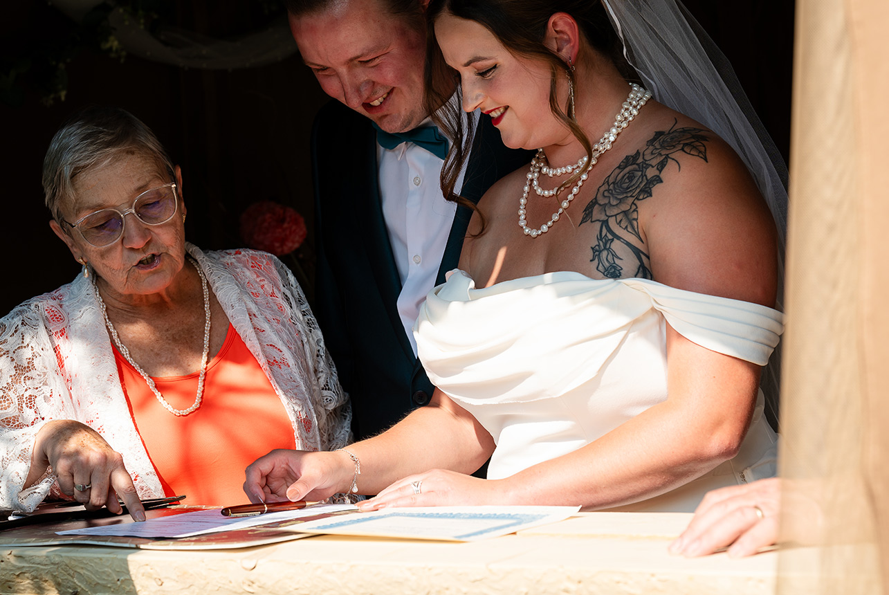 The commissioner guides the bride as she signs the marriage certificate, with her groom looking over her shoulder