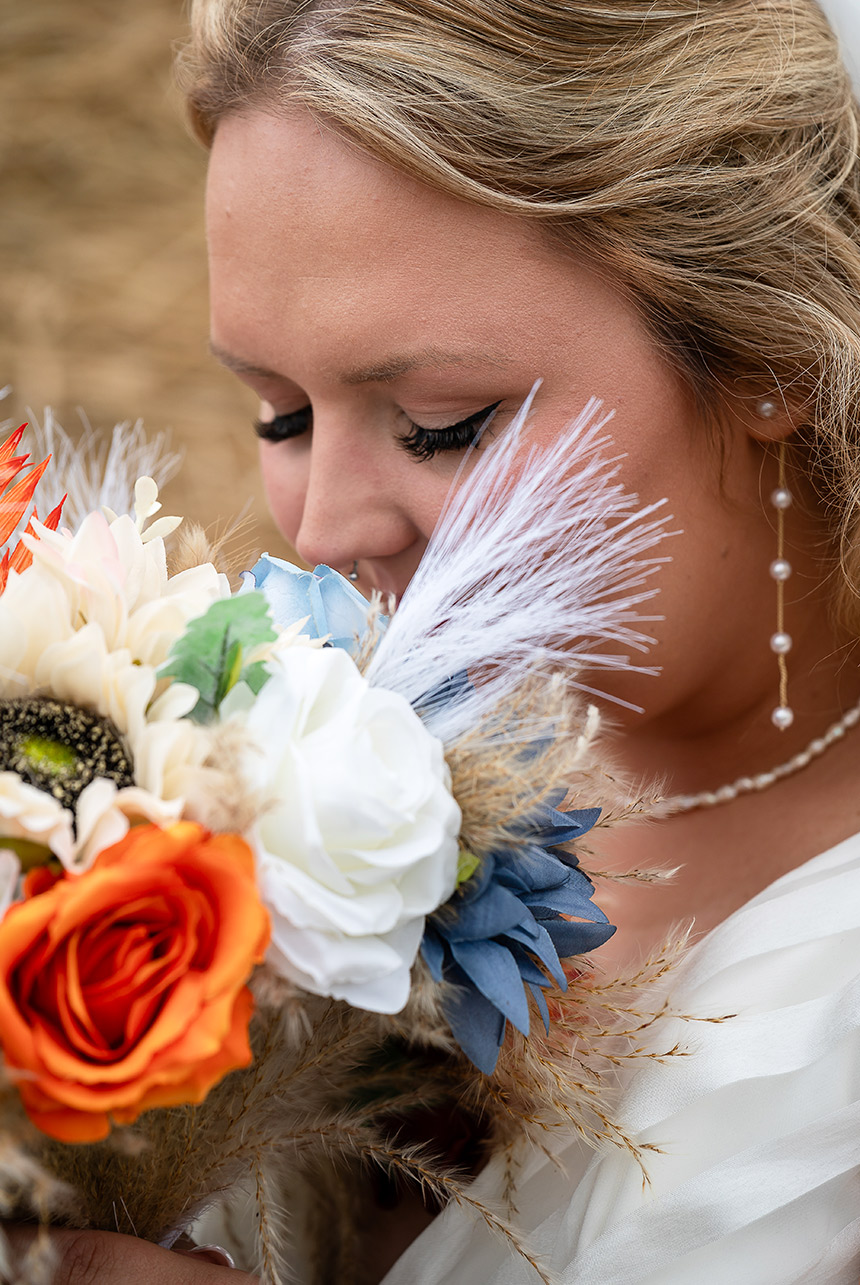 Bride with closed eyes, smelling her bouquet in hand, with autumn leaves in the blurred background