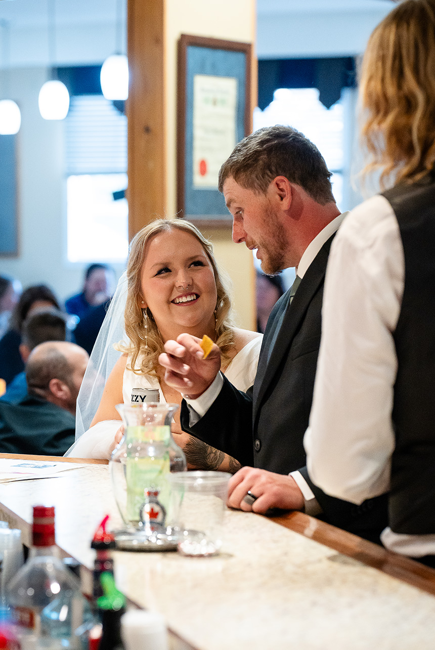 Bride smiling as she looks up at the groom at the bar inside the Royal Canadian Legion in Redwater