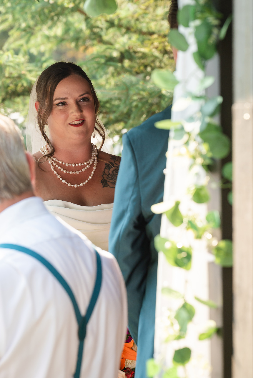 Bride looks up at her groom with a proud smile, framed by the warm summer light from the open side of the ceremony stage