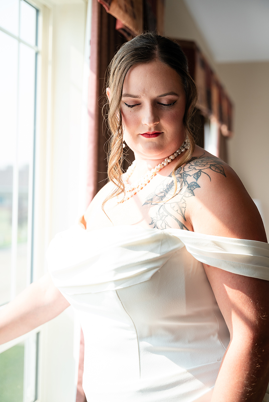 Bride closes her eyes peacefully as the sunlight bathes her, revealing her floral tattoo and elegant wedding gown