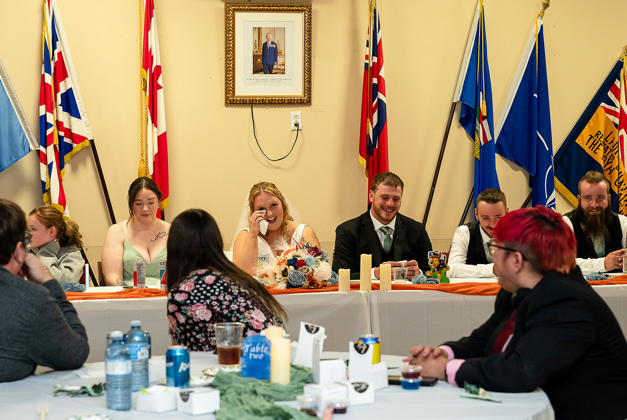 Bride laughing and wiping away a tear as the wedding party shares a joyful moment at the reception
