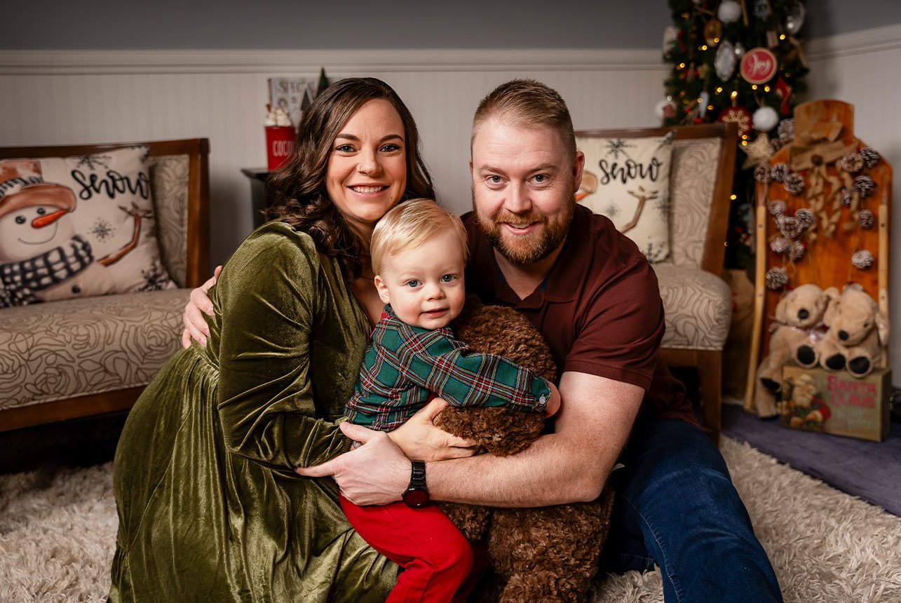 Smiling family of three with their Teddy bear during a warm, indoor Christmas mini session.