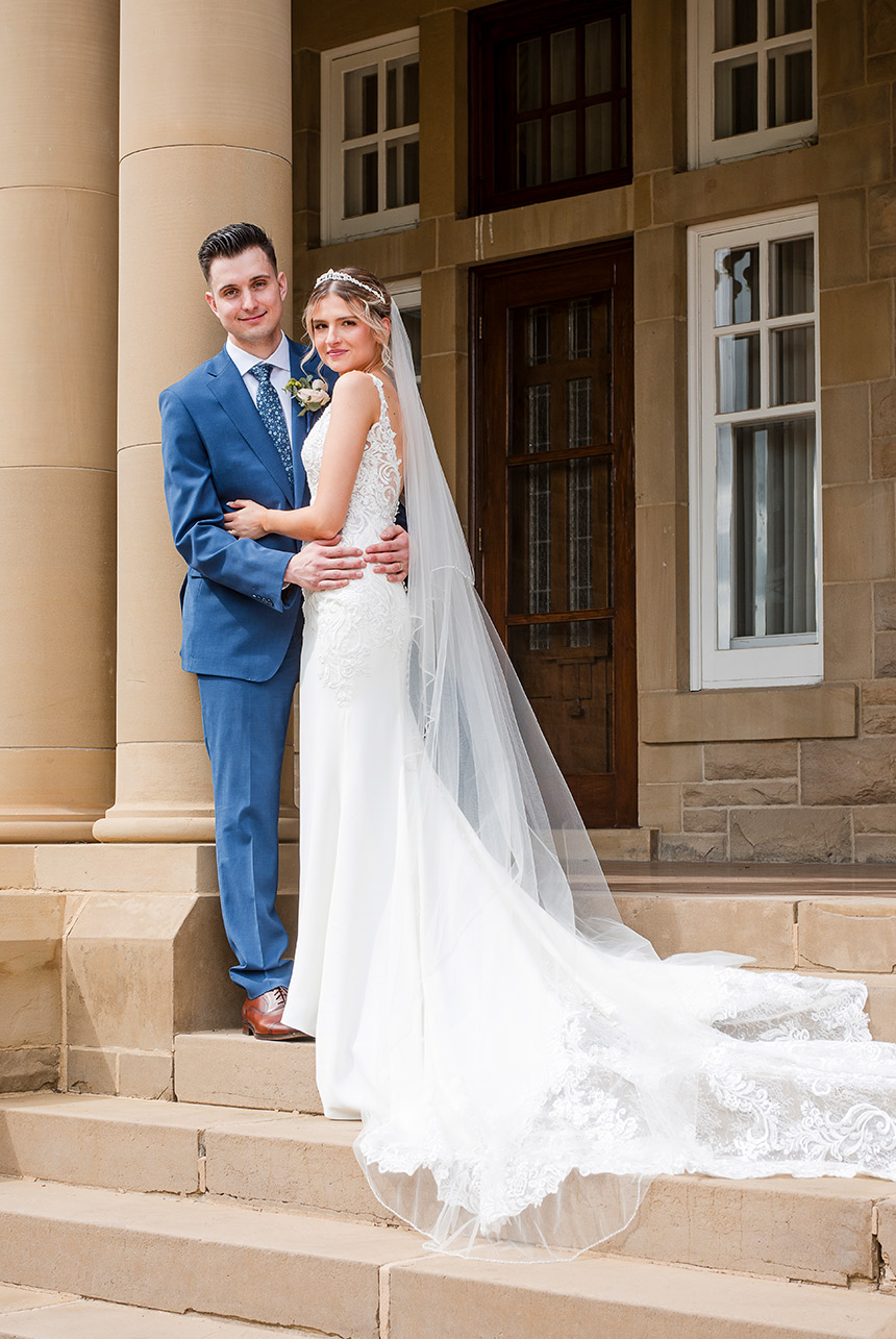 Bride and groom stand on stone steps, long lace veil trailing as they hold each other