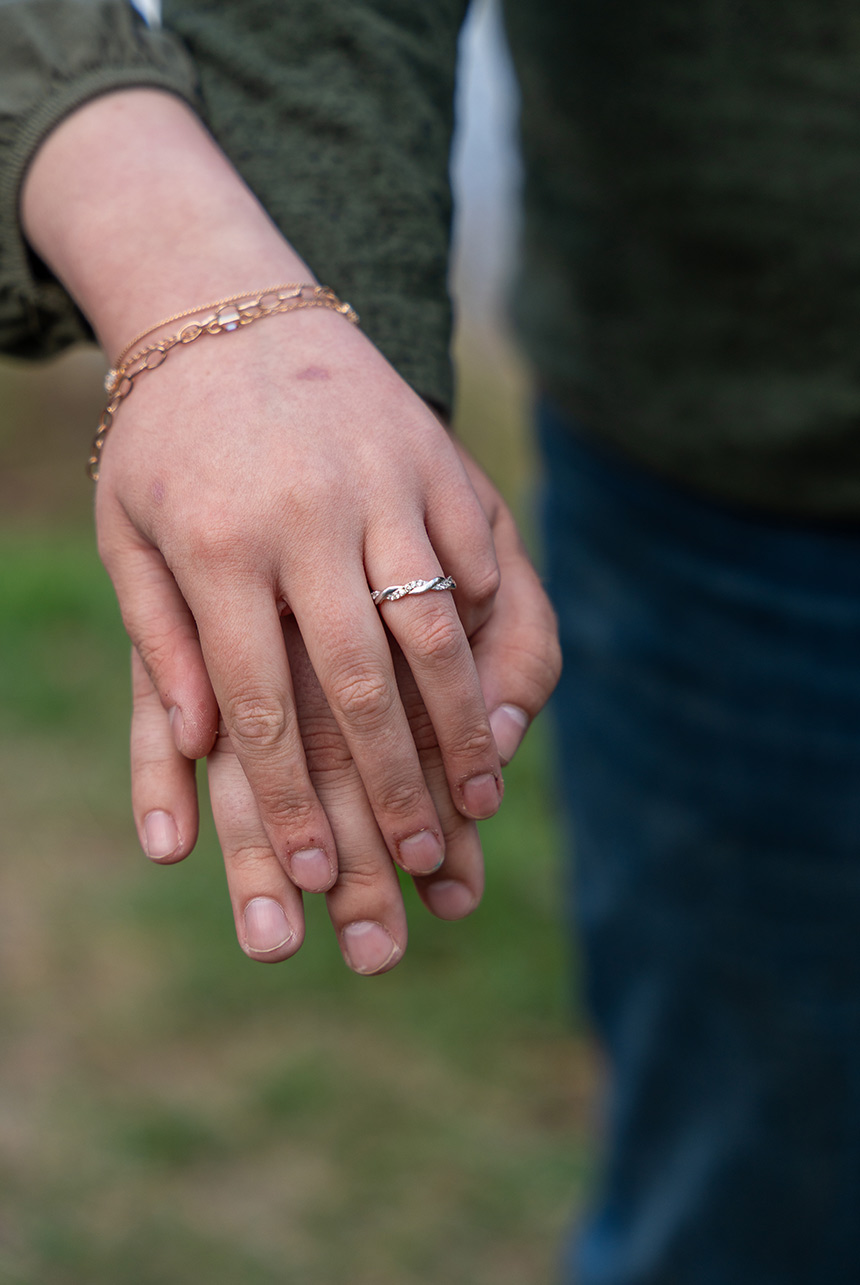 Close-up of hands gently intertwined, showcasing a delicate engagement ring and bracelet during spring session