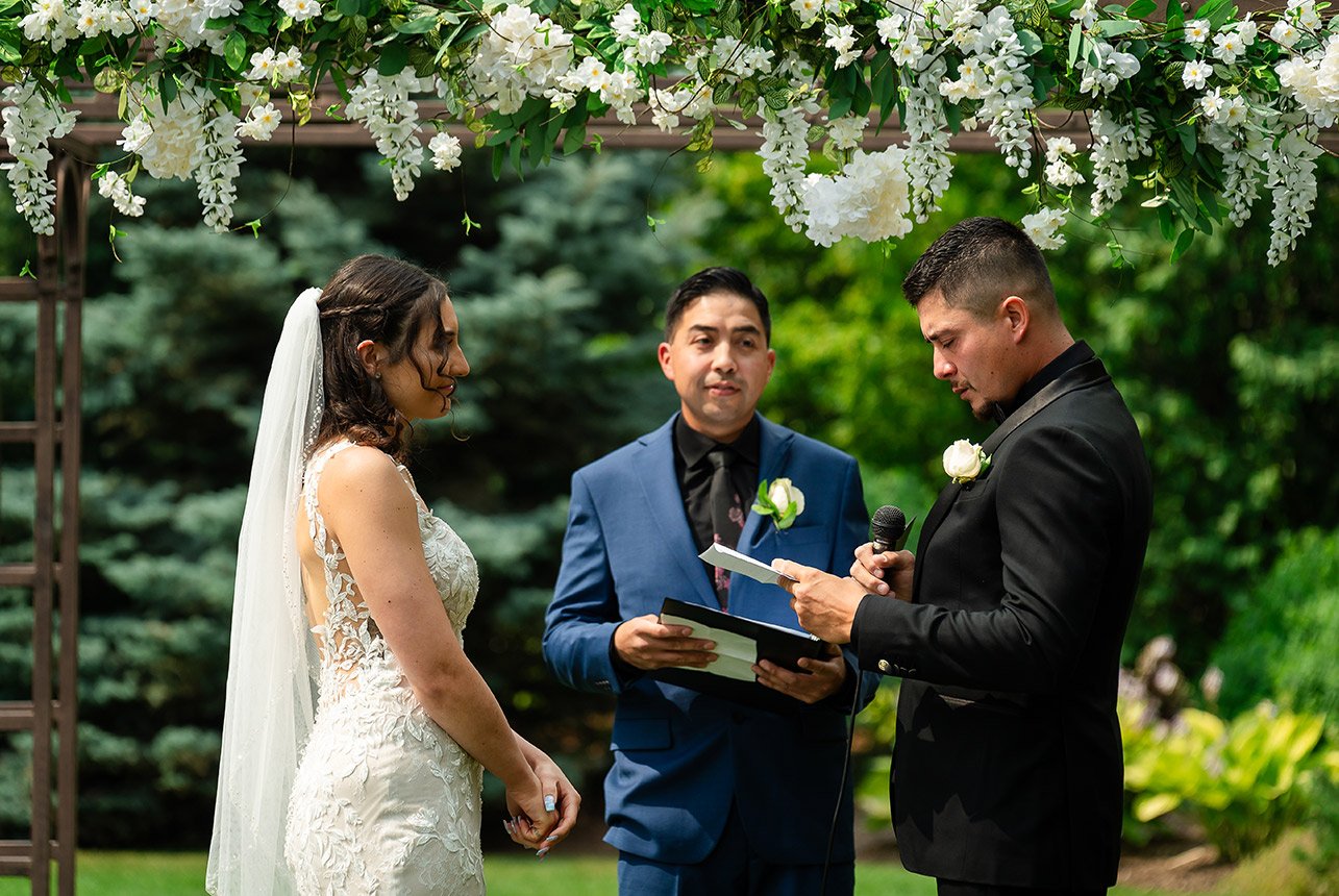Wedding commissioner in the center as the groom holds a microphone and notes, preparing to read his vows during the ceremony.