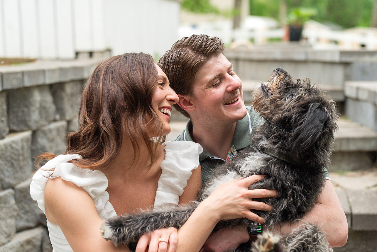 couple cuddling dog engagement photo stairs Couple sits on stone steps laughing while holding their fluffy black and white dog