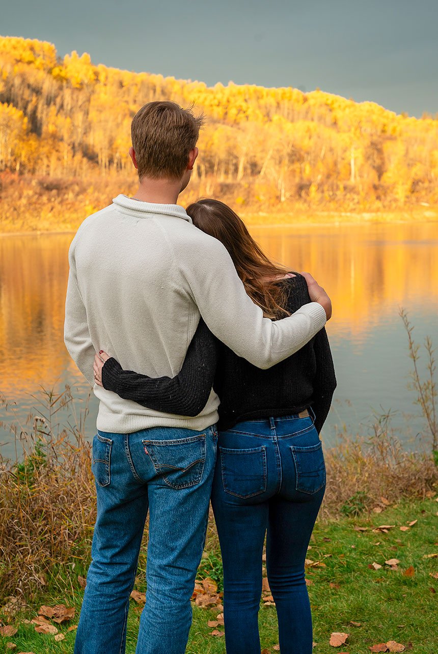 Couple embracing by the river during an autumn session in Devon, Alberta