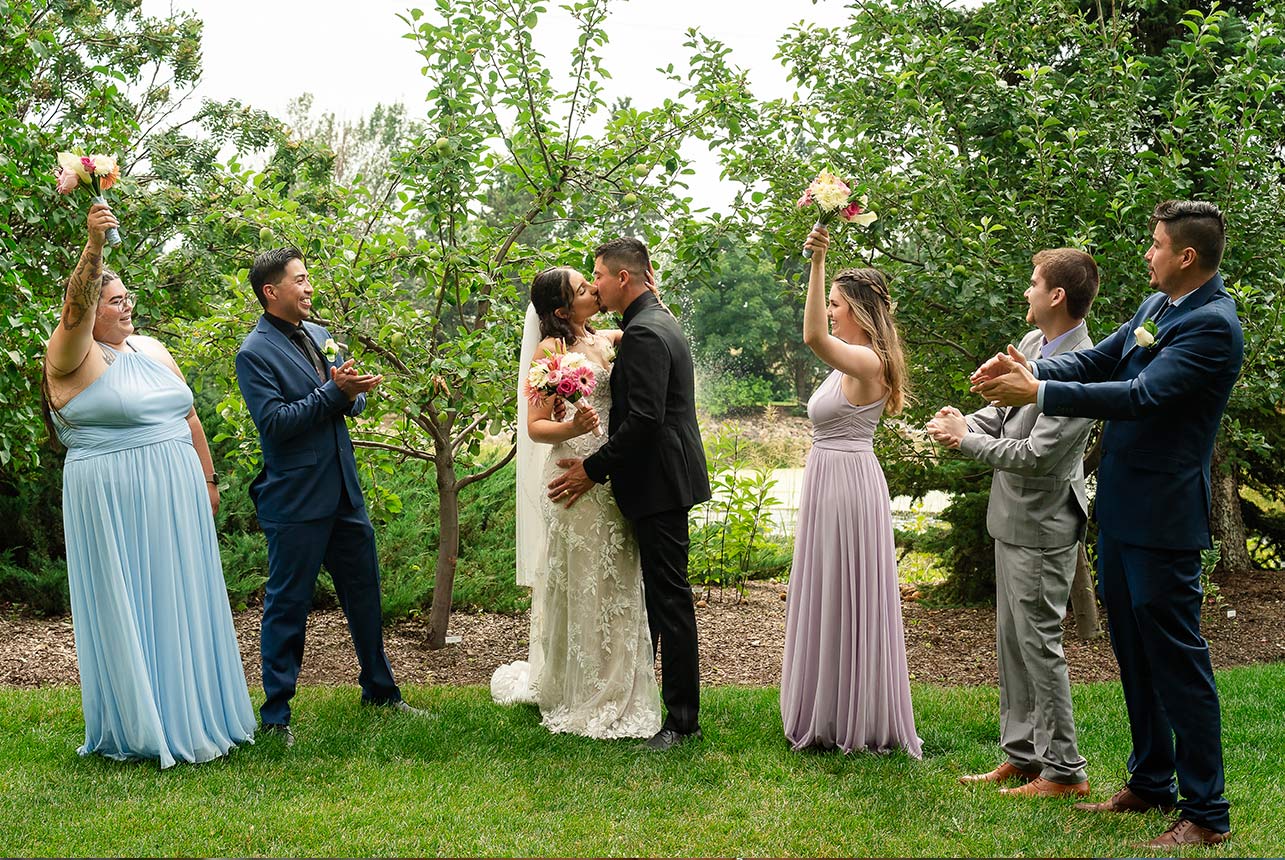 A couple sharing a kiss as their wedding party cheers and claps in approval during their ceremony at Greenland Botanic Gardens in Sherwood Park, near Edmonton.