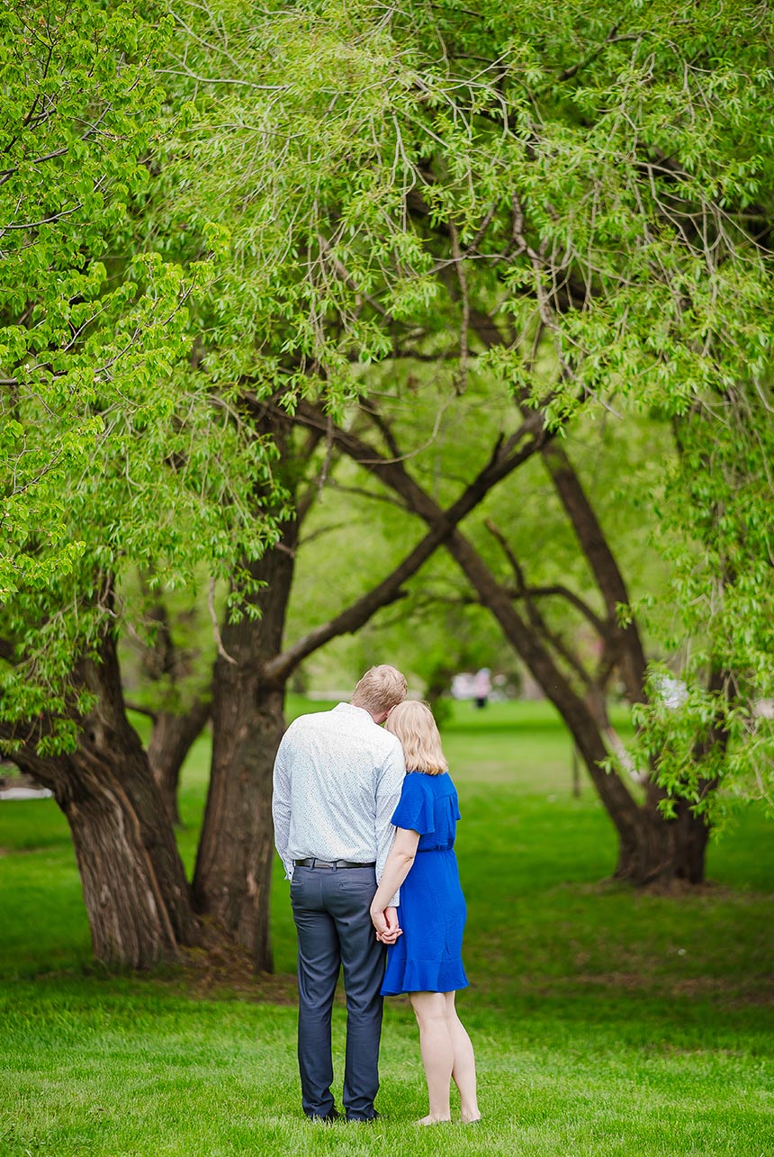 Couple snuggling and holding hands, looking up at the canopy of newly awakened trees in the park