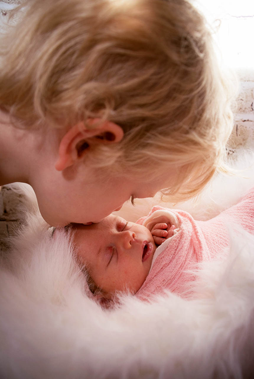 Curly blonde hair brother kissing his newborn sister