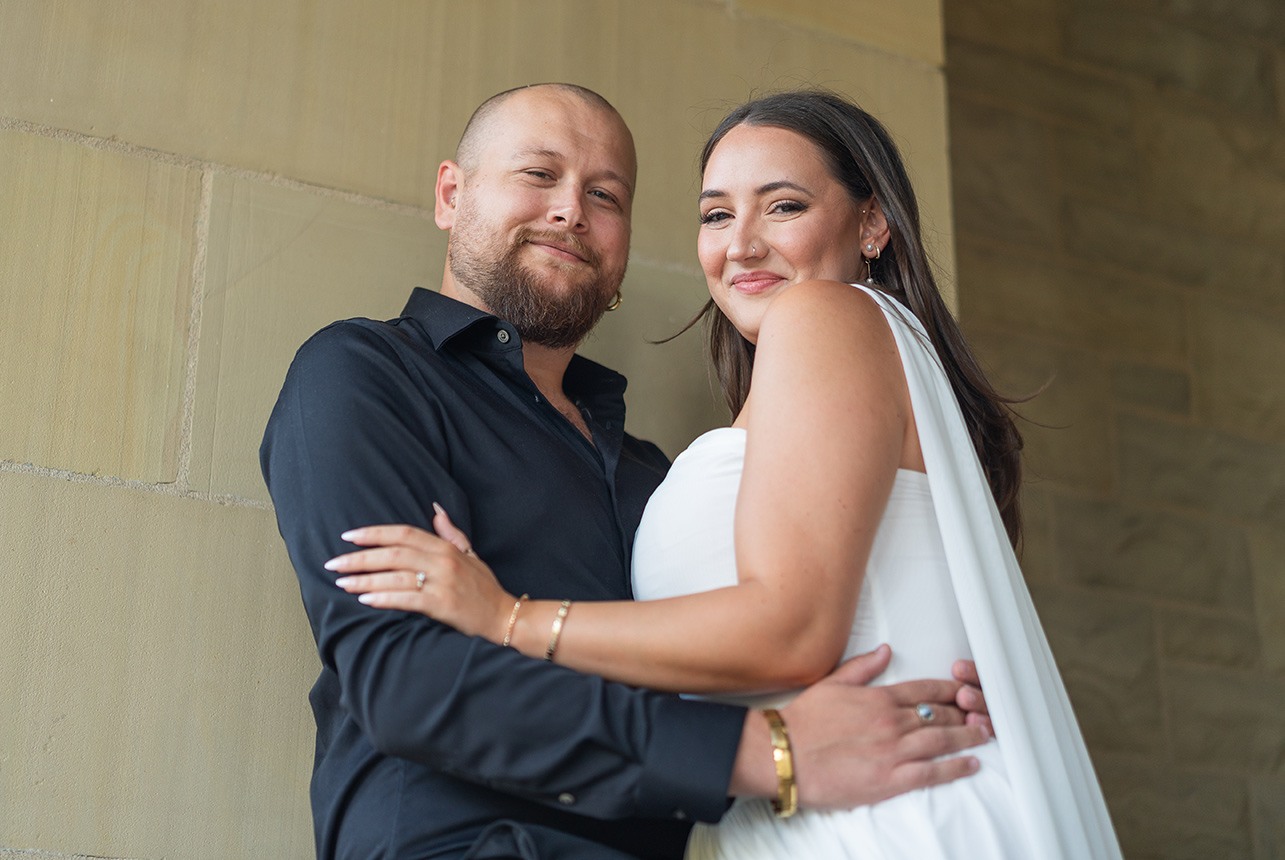 Smiling couple in elegant attire embracing by a stone wall; photography pricing and packages in Edmonton