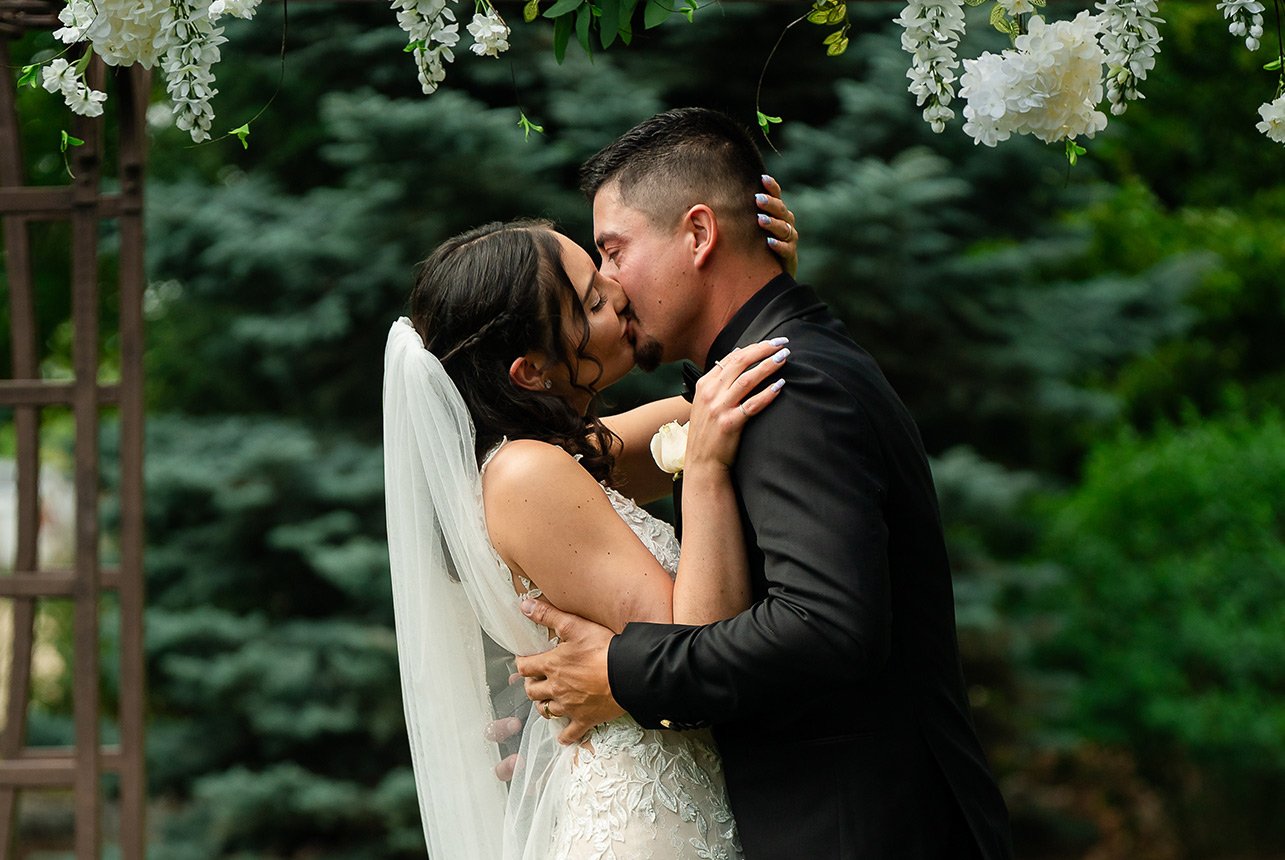 Bride and groom share their first kiss, her hands cupping his head during an outdoor ceremony in Edmonton