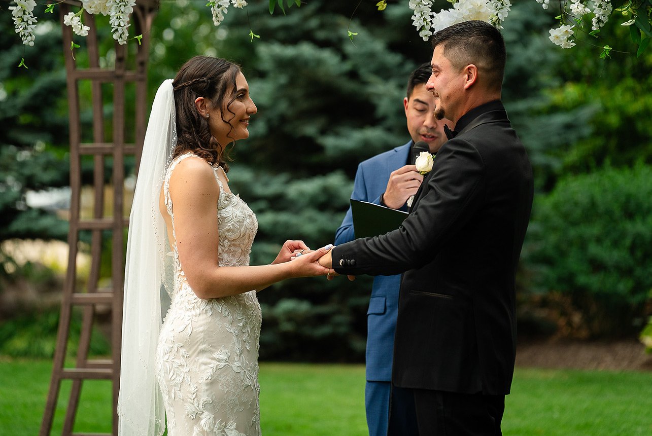 Bride placing the wedding ring on the groom’s hand at an outdoor summer ceremony in Edmonton