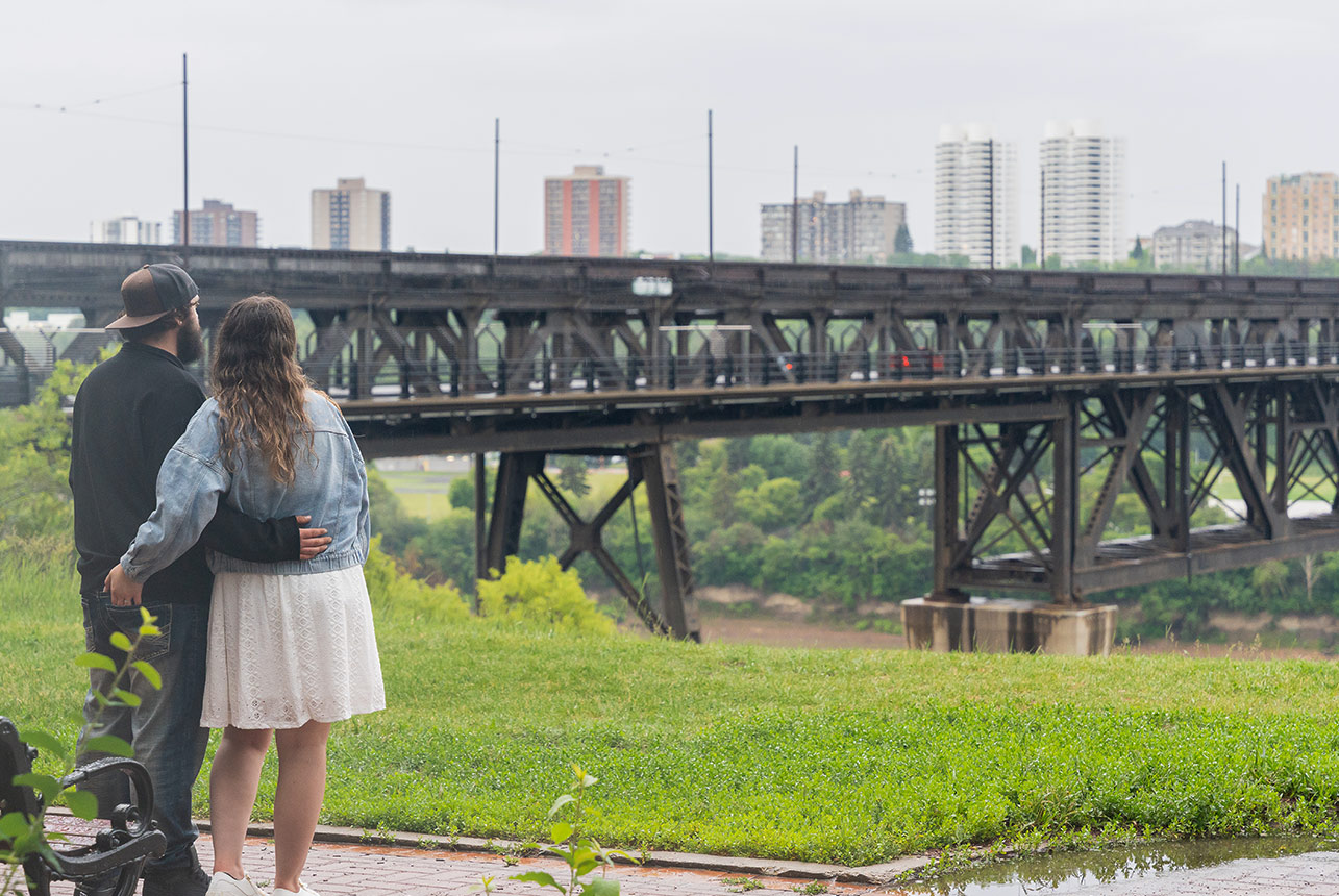 Couple looks out toward Edmonton’s High Level Bridge during rainy engagement session